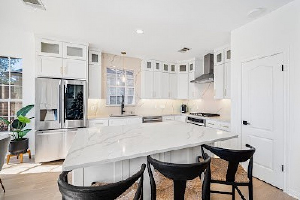 Modern kitchen remodel featuring gray custom cabinets, a large white island with a gold faucet, marble backsplash, stainless steel appliances, and pendant lighting – by Cabinet IQ kitchen remodelers.